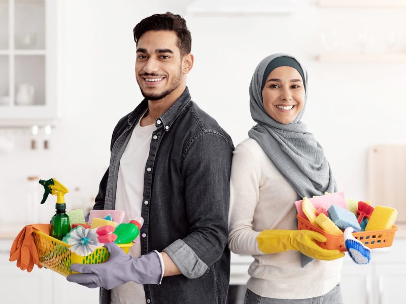 Happy muslim family cleaning their new apartment Happy muslim family cleaning their new apartment, holding house-keeping supplies and standing back to back in white kitchen, smiling at camera, copy space. House-keeping, apartment cleaning concept