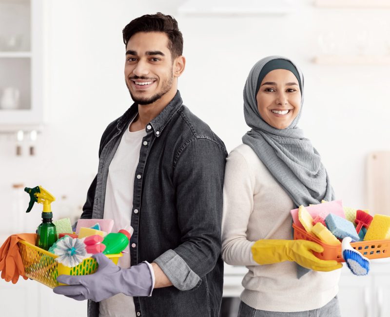 Happy muslim family cleaning their new apartment Happy muslim family cleaning their new apartment, holding house-keeping supplies and standing back to back in white kitchen, smiling at camera, copy space. House-keeping, apartment cleaning concept