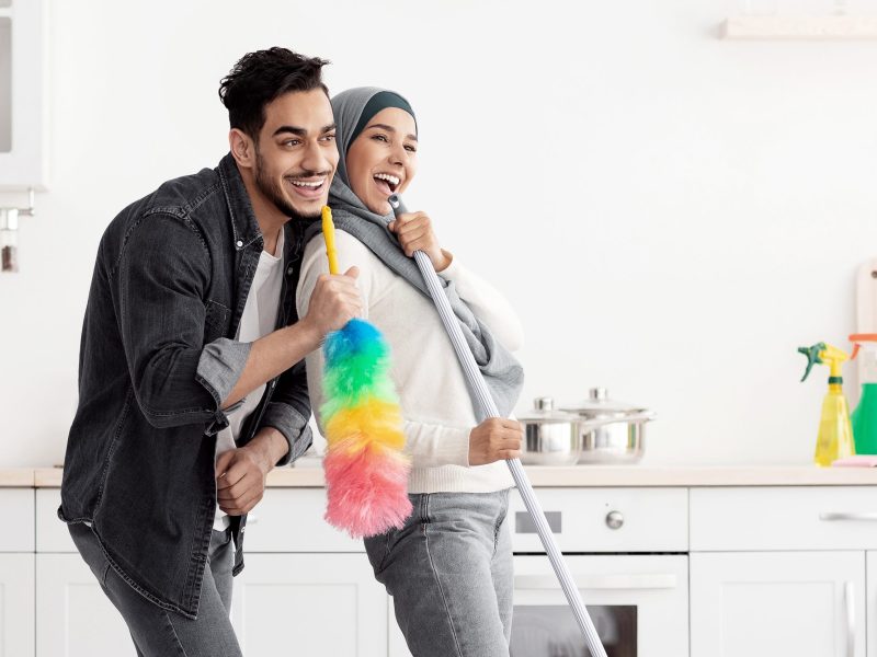 Joyful muslim couple cleaning floor and having fun in kitchen Beautiful joyful muslim young couple cleaning floor and having fun in kitchen together, full length photo, copy space. Funny lady in hijab and her singing boyfriend house-keeping their new house