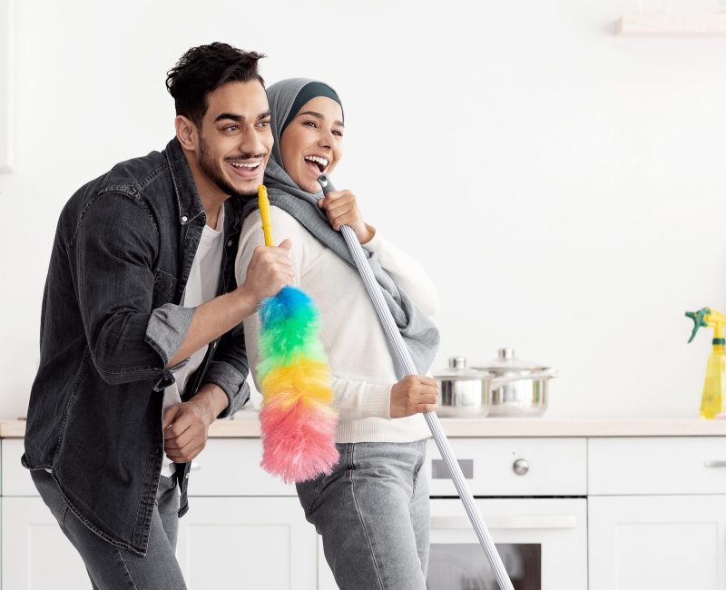 Joyful muslim couple cleaning floor and having fun in kitchen Beautiful joyful muslim young couple cleaning floor and having fun in kitchen together, full length photo, copy space. Funny lady in hijab and her singing boyfriend house-keeping their new house
