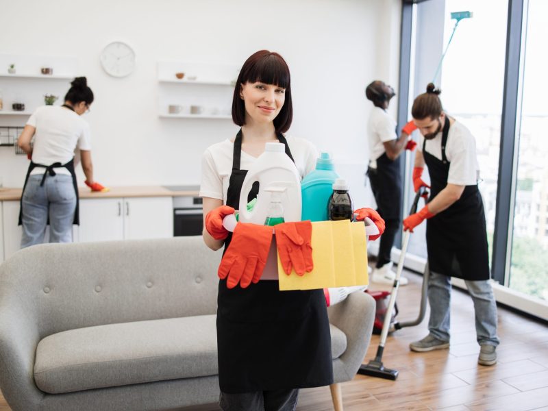 Young woman professional cleaning worker holding a bucket with detergents Portrait of young Caucasian woman professional cleaning worker holding a bucket for washing with detergents on bright kitchen studio background, copy space.