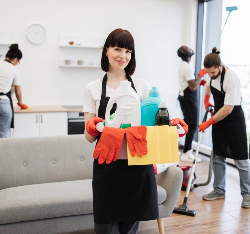 Young woman professional cleaning worker holding a bucket with detergents Portrait of young Caucasian woman professional cleaning worker holding a bucket for washing with detergents on bright kitchen studio background, copy space.